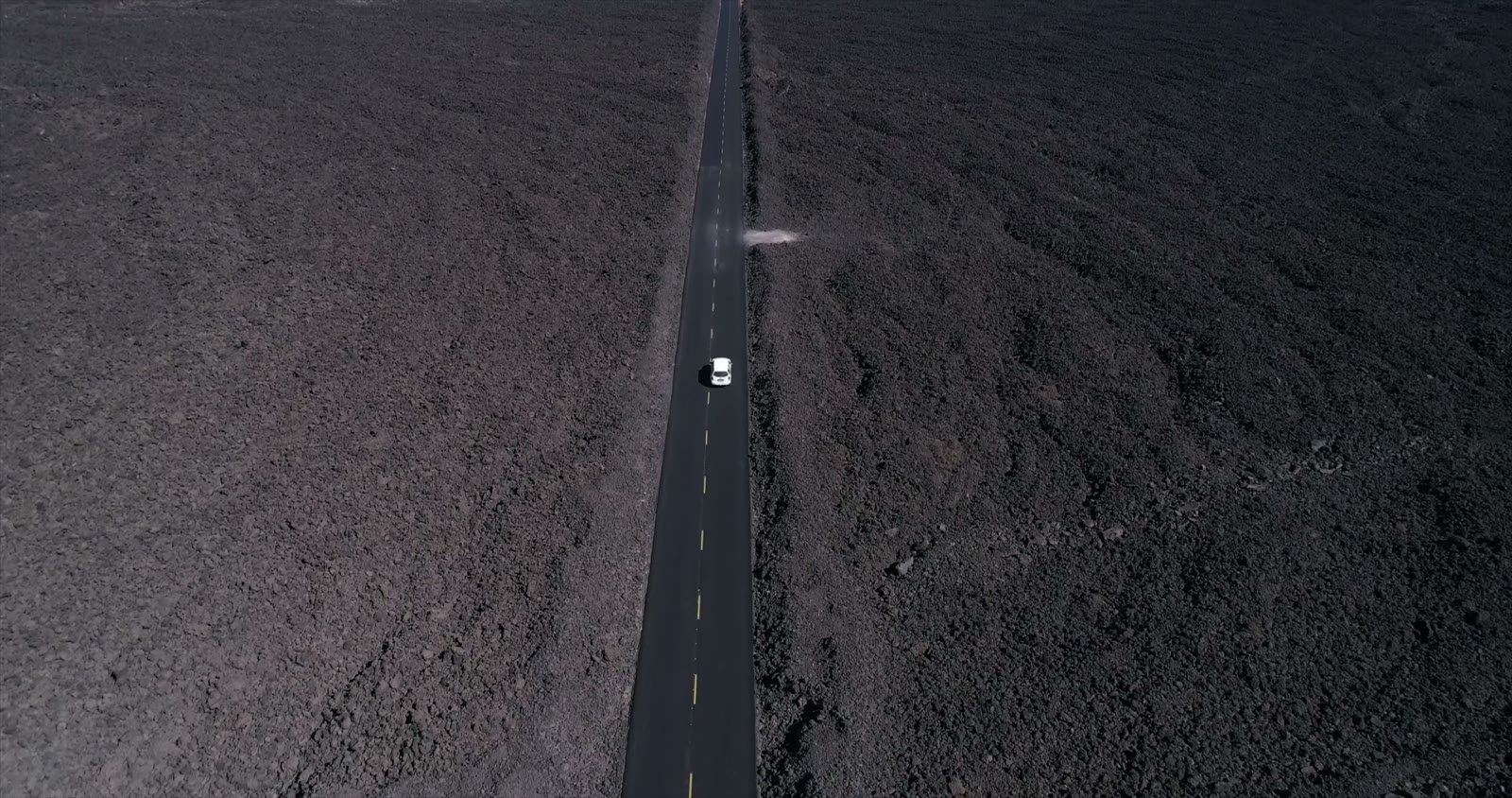 Aerial view of a lone car driving a long desert highway.